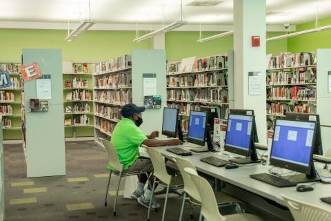 person sits at computer with book stacks behind them