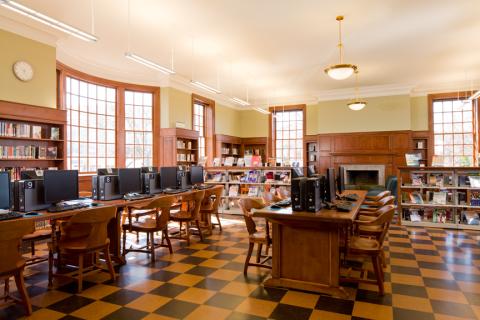 Large room with bookshelves and long tables with computer stations