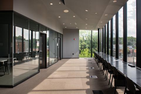 sunlit hallway with meeting rooms on the left and chairs looking out the window on the right