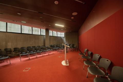 Lecture room with red carpet, a podium, and rows of black chairs