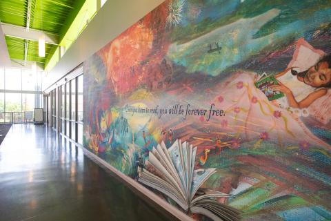 painted mural on wall of little girl lying down reading with the words "Once you learn to read you will be forever free"
