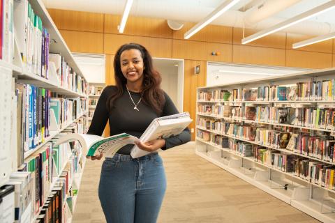 Woman smiling standing among bookshelves in the library