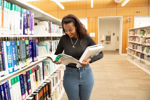 Woman holding books in one arm and reading another book in her other hand