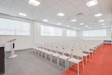 room with red carpet and white chairs set up in rows in front of a podium