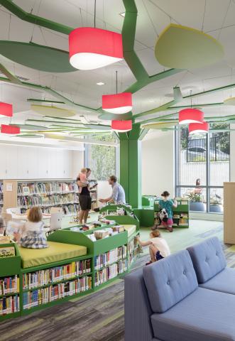 families in a children's reading room with green accents and red hanging lamps
