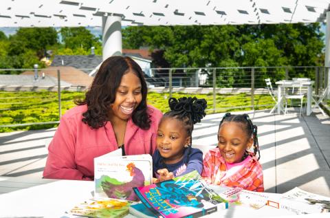 Family of a caregiver and two children sitting outside of the library reading and laughing together