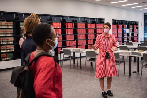 woman in red dress speaks to a group standing in front of her