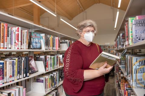 Older woman stands among book shelves holding a book 