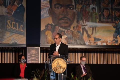 Man stands at a podium with a large mural of Martin Luther King Jr. behind him