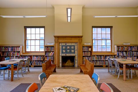 room with reading tables and a fireplace with a wooden mantle 