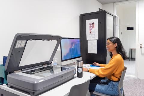 Woman sits at a table with a computer and large scanner