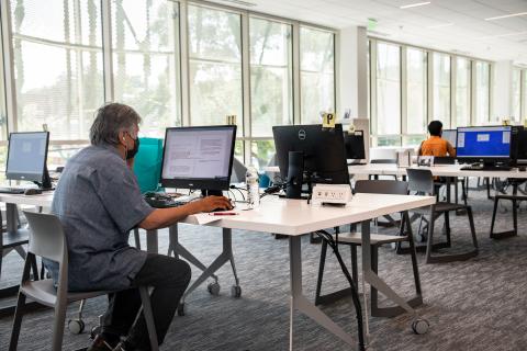 Older man sits at a computer with headphones in