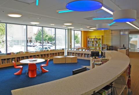 children's room with blue carpet, low book shelves, and low red plastic tables