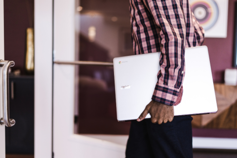 person carrying a chromebook under their arm by their side