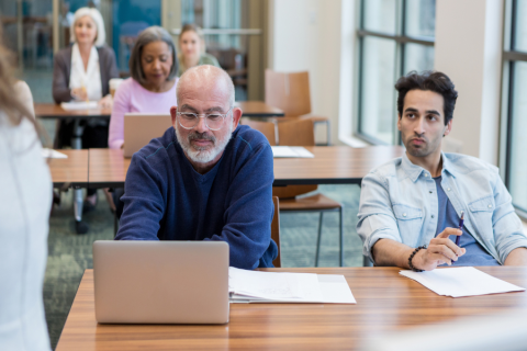 Classroom setting of adults, focused on a table with an older man and younger man sitting next to eachother