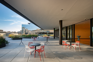 round tables with red and white chairs sit under the awning on the MLK rooftop