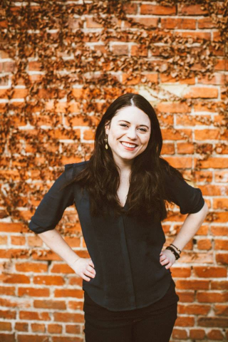 Morgan Elwell, a woman with long dark hair in front of a brick wall