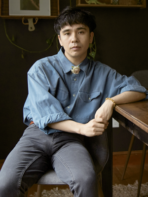 photographic portrait of ocean vuong, a young man in blue shirt and gray pants