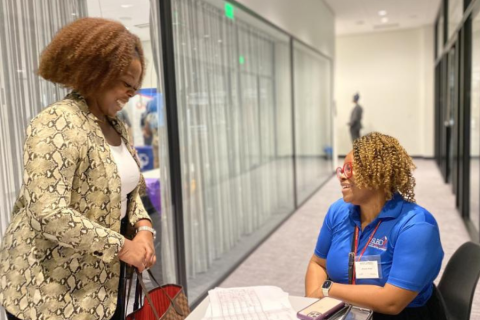 two women smile at each other at a check-in table for an event