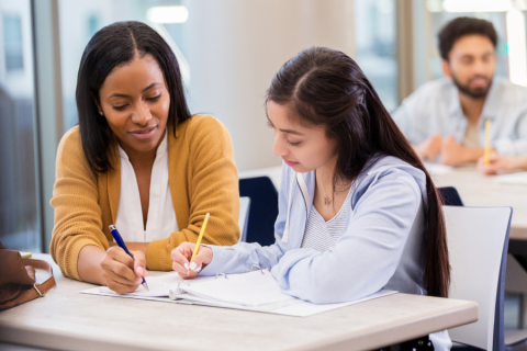 two women sitting at a desk with a binder