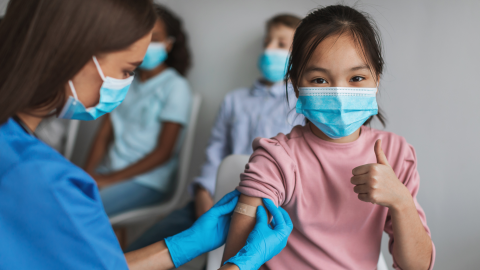 Child giving the thumbs up as a Dr. puts a bandaid on their arm after getting vaccinated 